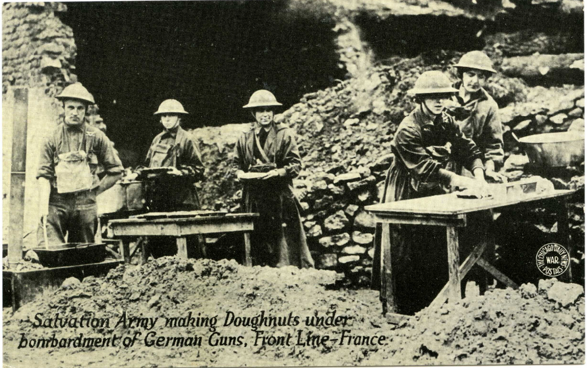 Five soldiers making dougnuts in a bombarded area of France.  A typeset footer reads "Salvation Army Making Doughnuts under bombardment of German Guns, Front Line, France."