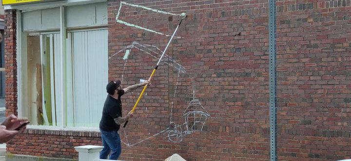 A man with a large roller paints on a brick wall.