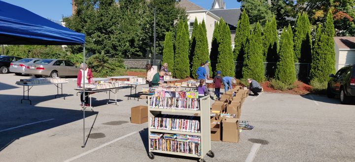 Multiple people surround tables and boxes during a book sale in a parking lot.